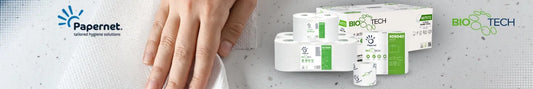 Werbebanner der Marke Papernet. Links ist eine Hand zu sehen, die ein weißes Papiertuch benutzt. Darüber das Papernet-Logo mit dem Slogan „tailored hygiene solutions“. Rechts im Bild befinden sich mehrere Rollen Papierhandtücher und eine Produktverpackung mit grünem Etikett der Linie „BIO TECH“. Oben rechts ist das grün-blaue „BIO TECH“-Logo mit stilisierten Molekülen zu sehen. Der Hintergrund ist hellgrau mit feiner Textur.