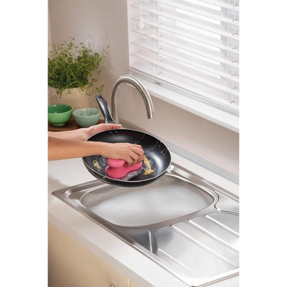 Ένα άτομο καθαρίζει ένα τηγάνι κάτω από τρεχούμενο νερό σε μια σύγχρονη κουζίνα με ένα Scotch-Brite® Delicate Color Comfort μη γρατζουνιστικό σφουγγάρι καθαρισμού (2 τεμάχια) από την 3M Deutschland GmbH - ιδανικό για ευαίσθητες επιφάνειες. Πράσινα μπολ και ένα φυτό βρίσκονται στον πάγκο.