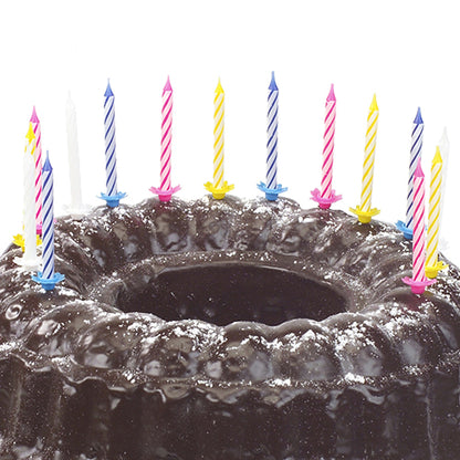 Ένα σοκολατένιο κέικ πασπαλισμένο με ζάχαρη άχνη και διακοσμημένο με δέκα PAPSTAR κεριά γενεθλίων 6 εκ., χρωματιστά ταξινομημένα με βάση (από PAPSTAR GmbH) σε διάφορα χρώματα.