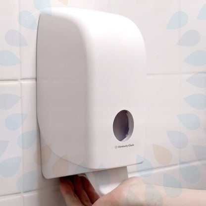 Μια κασέτα Kleenex® Απαλό Λοσιόν Καθαρισμού της Kimberly-Clark GmbH (διαφανής, 1 L) απεικονίζεται σε έναν λευκό κεραμικό τοίχο, με ένα χέρι που τραβάει μια πετσέτα από το κάτω μέρος και ένα μικρό στρογγυλό παράθυρο στο μπροστινό μέρος. Διατίθεται σε συσκευασίες με 6 κασέτες.