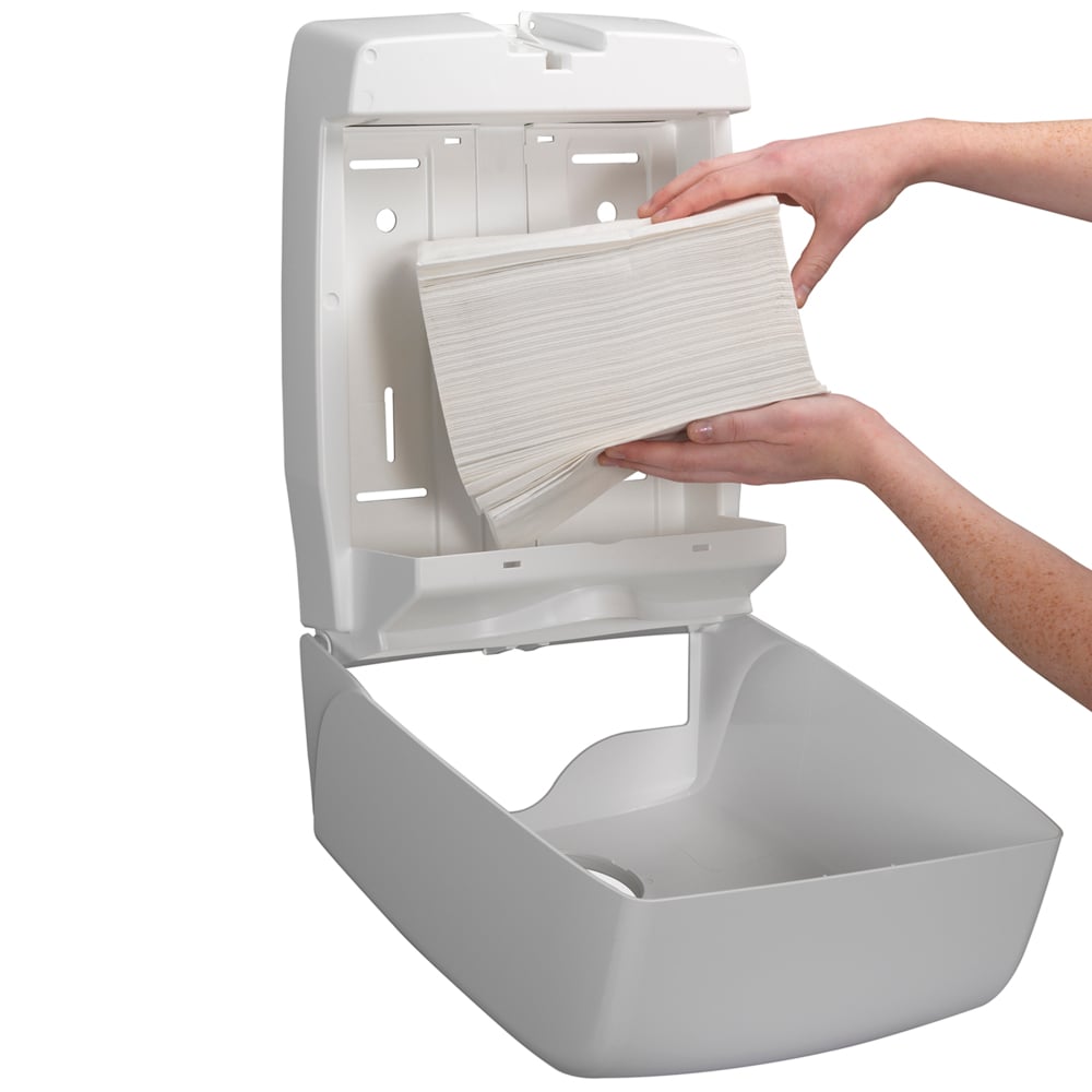 Eine Person füllt einen an der Wand montierten Spender mit Kleenex® Ultra™ Falthandtüchern Interfold Weiß (15 Clips x 96 Blatt) der Kimberly-Clark GmbH nach und sorgt für hygienisches Händetrocknen, da der geöffnete Spender ein einfaches Nachfüllen ermöglicht.