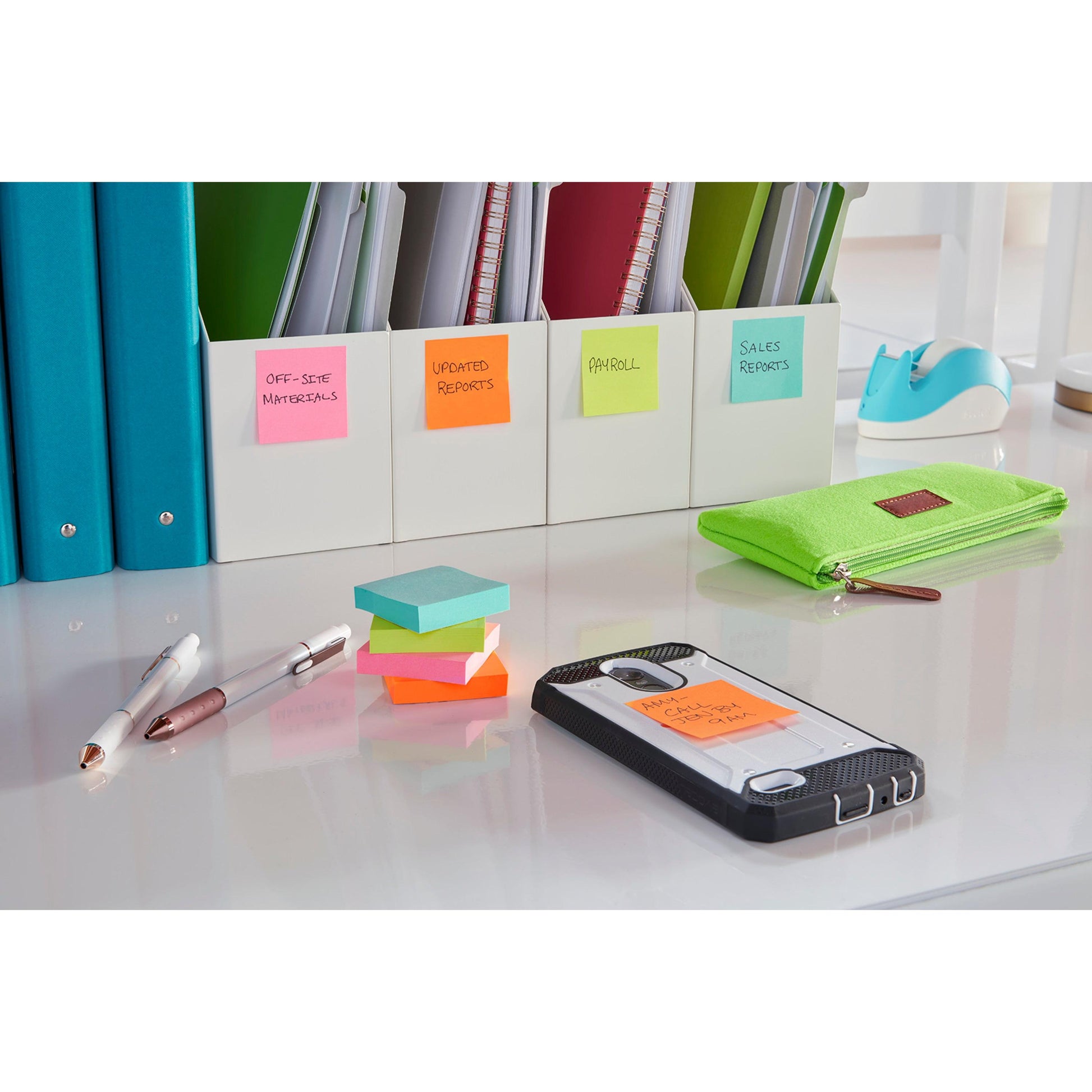 Auf dem aufgeräumten Schreibtisch liegen beschriftete Ordner, ein grünes Mäppchen, zwei Stifte und ein Smartphone mit einer Post-it® Super Sticky Note (76x127 mm, 3M Deutschland GmbH), auf der "AM Call Client Chet" steht. Die gut beleuchtete Oberfläche ist weiß.