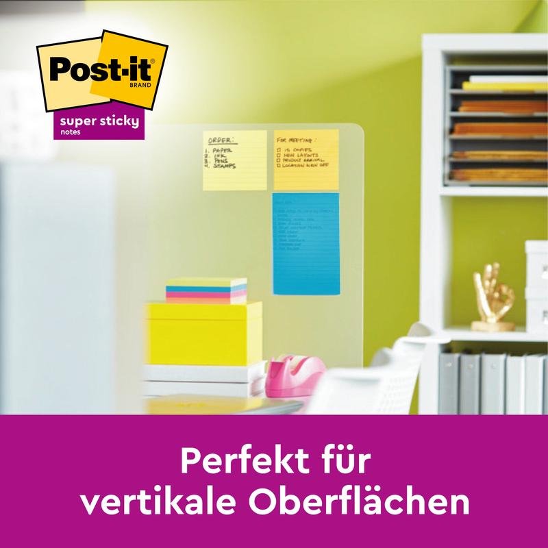 Σε έναν γυάλινο τοίχο κολλάνε Post-it® Super Sticky Meeting Notes από την 3M σε διάφορα χρώματα (203 x 153 mm, 70 φύλλα/μπλοκ, 3 μπλοκ), ιδανικά για κάθετες επιφάνειες. Στο παρασκήνιο υλικά γραφείου και βιβλία στο γραφείο.