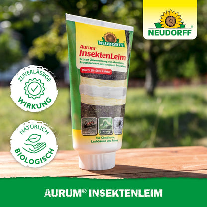 Ένας σωλήνας κόλλας εντόμων Aurum από το Neudorff Shop στέκεται σε ένα τραπέζι σε εξωτερικό χώρο. Η συσκευασία τονίζει την αξιόπιστη δράση κατά των μυρμηγκιών και των πεταλούδων του χειμώνα και προστατεύει τα οπωροφόρα δέντρα με φυσικά, βιολογικά συστατικά.