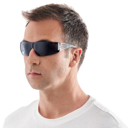 Ένας άντρας με κοντά καστανά μαλλιά, σε ένα λευκό T-shirt, φοράει τα γυαλιά ασφαλείας 3M™ SecureFit™ 200 από την 3M Deutschland GmbH, ελαφρώς στραμμένος προς τα αριστερά σε ένα απλό λευκό φόντο.