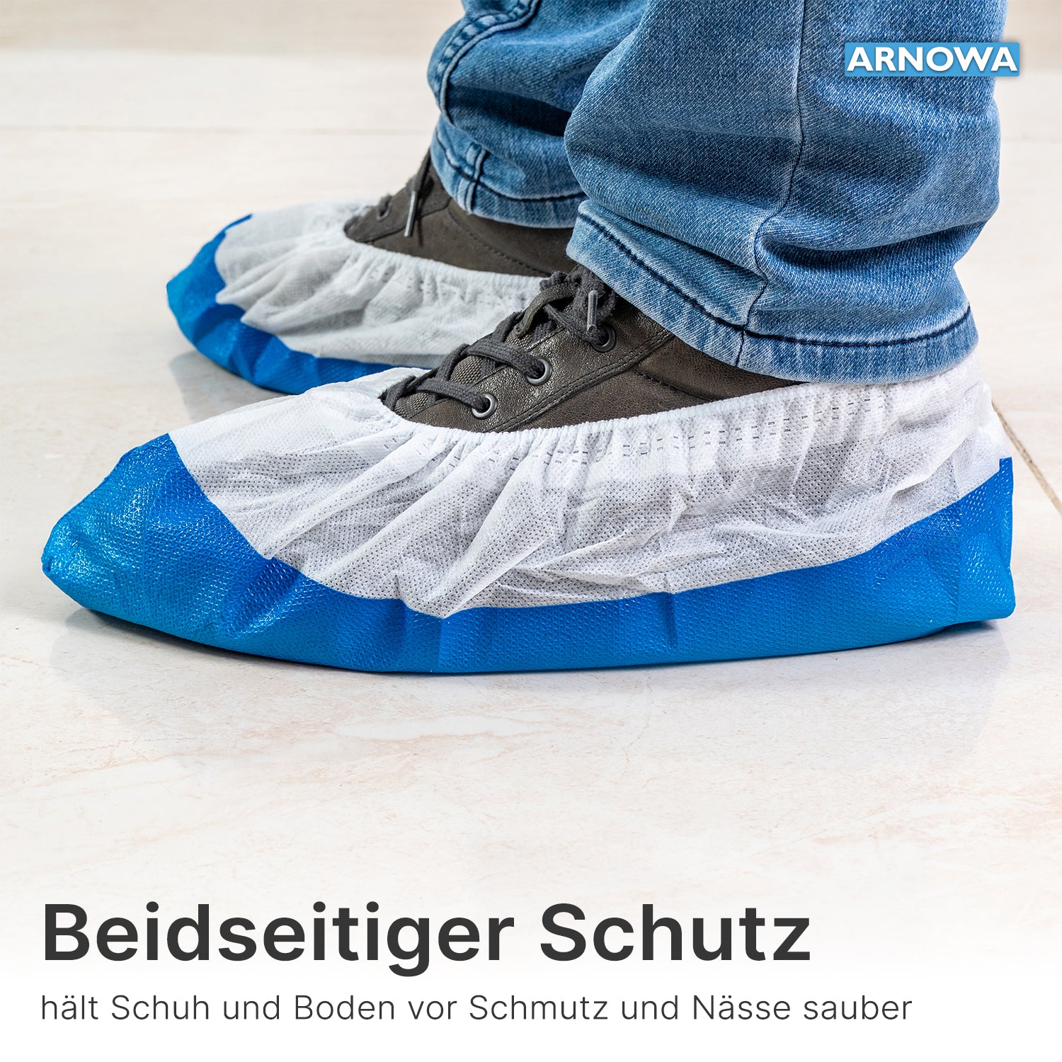 Person trägt ARNOMED CPE/PP Schuhüberzieher von ARNOWA GmbH, wasserdicht und in Blau-Weiß, über grauen Schuhen auf hellen Fliesen; Text und Branding sind sichtbar.