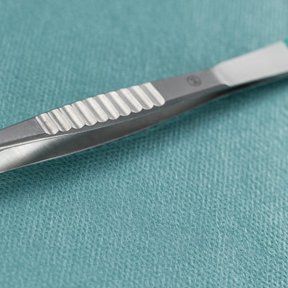 Μια κοντινή λήψη μιας λαβίδας διαχωριστή Hartmann της Paul Hartmann AG ευθεία 9cm, αποστειρωμένη (πακέτο με 40 κομμάτια), που βρίσκεται δίπλα σε ένα μεταλλικό χειρουργικό νυστέρι πάνω σε ένα ιατρικό πανί με υφή σε απόχρωση teal.