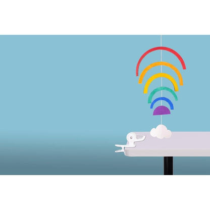 Ένα πολύχρωμο κινητό από χαρτί με πέντε ουράνια τόξα και ένα λευκό σύννεφο κρέμεται στην άκρη ενός λευκού τραπεζιού, ασφαλισμένο από τον διανομέα ταινίας Scotch™ Clip & Twist C19 με ταινία Magic™, μπροστά από ένα ανοιχτό γαλάζιο φόντο.