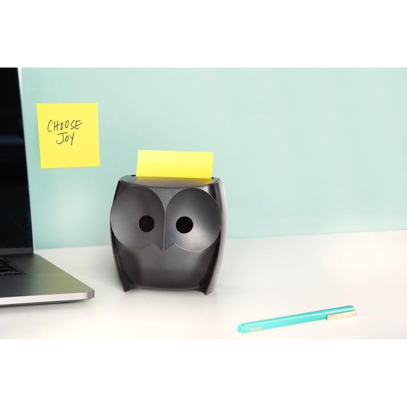 Ένας μαύρος διανομέας Post-it® Z-Zettel «Κουκουβάγια» (3M Deutschland GmbH) με κίτρινα Super Sticky Z-Zettel βρίσκεται σε ένα λευκό γραφείο, δίπλα ένας φορητός υπολογιστής και ένα μπλε στυλό. Στον τοίχο κρέμεται ένα χαρτί «CHOOSE JOY» μπροστά σε ανοιχτό μπλε φόντο.