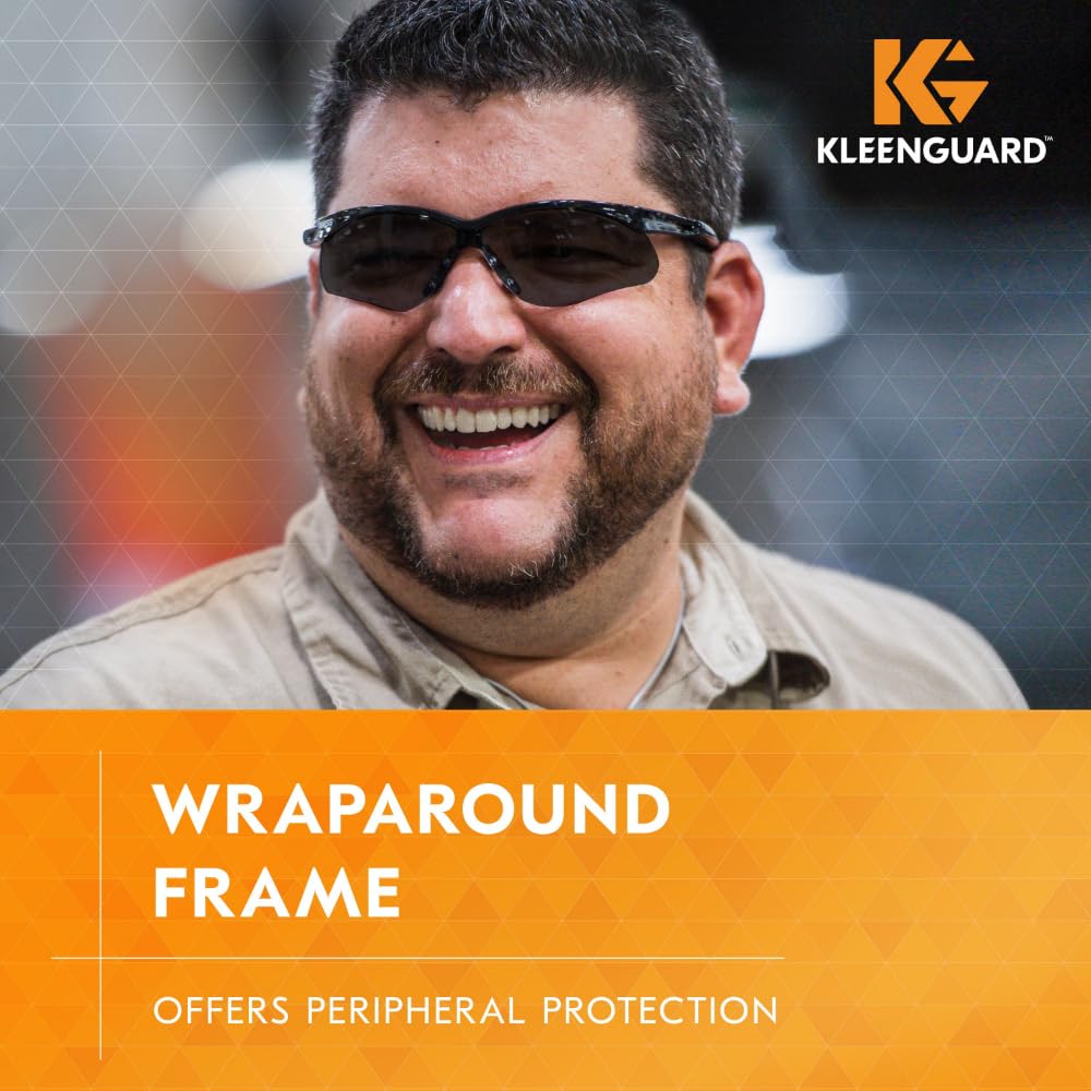 Ein bärtiger Mann mit dunkler KleenGuard® V30 Nemesis™ Schutzbrille - Smoke Spiegel von Kimberly-Clark GmbH lächelt. Das KleenGuard Logo ist oben rechts. Text: "Wraparound Frame - Bietet peripheren Schutz" auf orangefarbenem Hintergrund.
