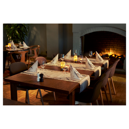 Ένας άνετος χώρος τραπεζαρίας διαθέτει δύο ξύλινα τραπέζια με ποτήρια κρασιού και πετσέτες Duni Bio Dunisoft® δίπλα σε τρεμοπαίζουσες κεριά. Σκούρες καρέκλες περιβάλλουν τα τραπέζια, αναβαθμισμένες από ένα αναμμένο τζάκι. Απαλές θέσεις και ένα φυτό συμβάλλουν στο σχέδιο εμπνευσμένο από τη φύση.