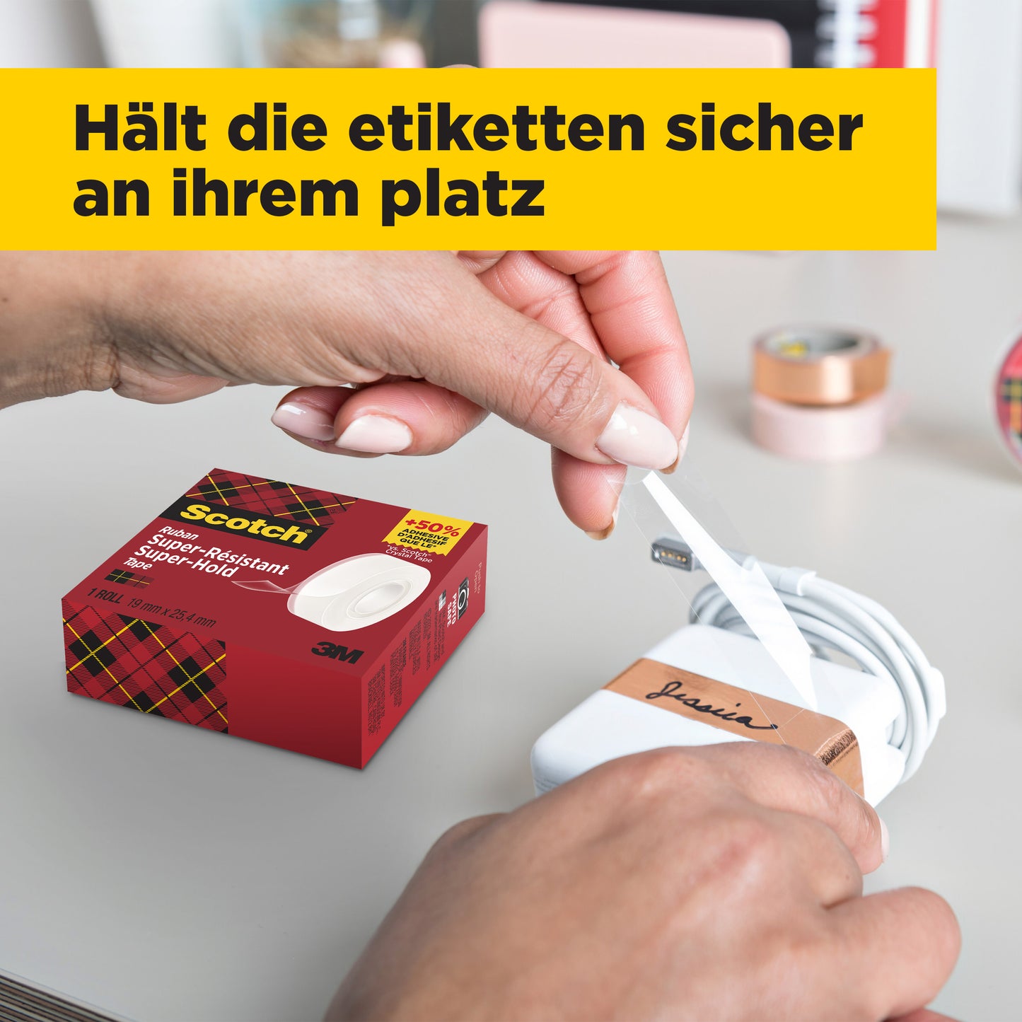 Eine Person wickelt ein weißes Etikett mit schwarzer Schrift um ein weißes Ladegerät, während auf dem Tisch eine Schachtel Scotch® Super-Hold Secure Tape, 1 Rolle, 19 mm x 25,4 m von 3M Deutschland GmbH steht. Im Hintergrund sind unscharfe Büromaterialien und eine gelbe deutsche Fahne zu sehen.