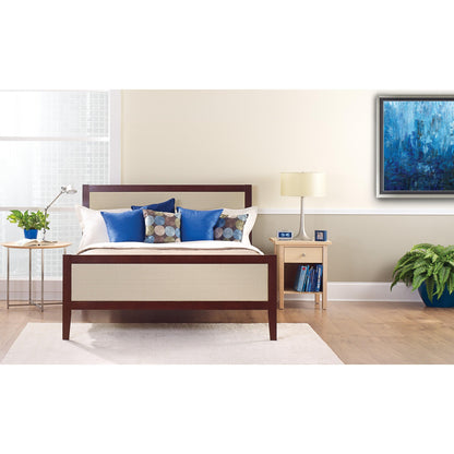 Ein ordentlich gemachtes Bett mit weißen und blauen Kissen steht vor einer hellen Wand, die mit ScotchBlue™ Malerabdeckband "Multi-Surface" der 3M Deutschland GmbH beklebt ist. Auf einem Nachttisch stehen eine Lampe, eine Uhr, Bücher und eine Topfpflanze neben dem hellen Fenster.