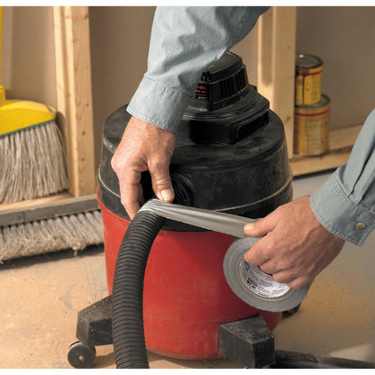 Eine Person, die ein langärmeliges Hemd trägt, verwendet 3M Deutschland GmbH Scotch® Universal Klebeband 2904 (25 m x 48 mm), um den Schlauch eines rot-schwarzen Werkstattsaugers zu befestigen. Im Hintergrund sind ein Besen und Farbdosen zu sehen.