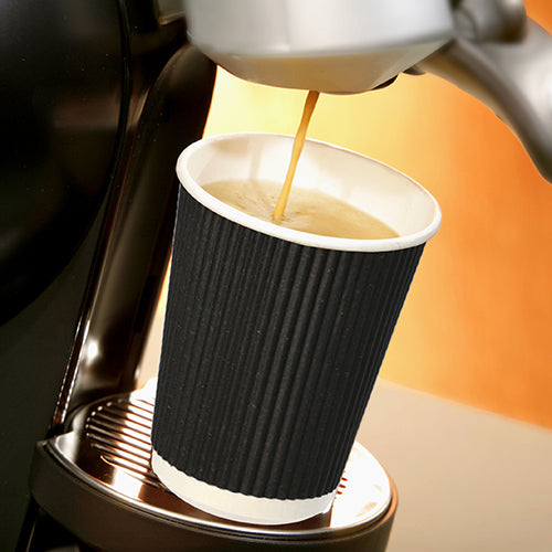 Ένα κύπελλο Starpak 25, χαρτί "To Go" Ripple Wall-Becher στέκεται σε μια μεταλλική πιατέλα στάλαξης κάτω από την έξοδο μιας καφετιέρας ενώ ζεστός καφές ρέει μέσα και αναδεικνύεται μπροστά σε ένα απαλά φωτισμένο, ζεστό φόντο.