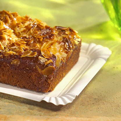 Στο PAPSTAR χάρτινο πιάτο τετράγωνο 13x20 cm, λευκό, "pure" για γιορτές (12 τεμάχια) από την PAPSTAR GmbH ακουμπάει ένα ορθογώνιο κέικ με ξυρισμένα αμύγδαλα - μια φιλική προς το περιβάλλον, κομψή δυνατότητα σερβιρίσματος σε μια φωτεινή επιφάνεια με πράσινο γυαλί πίσω.