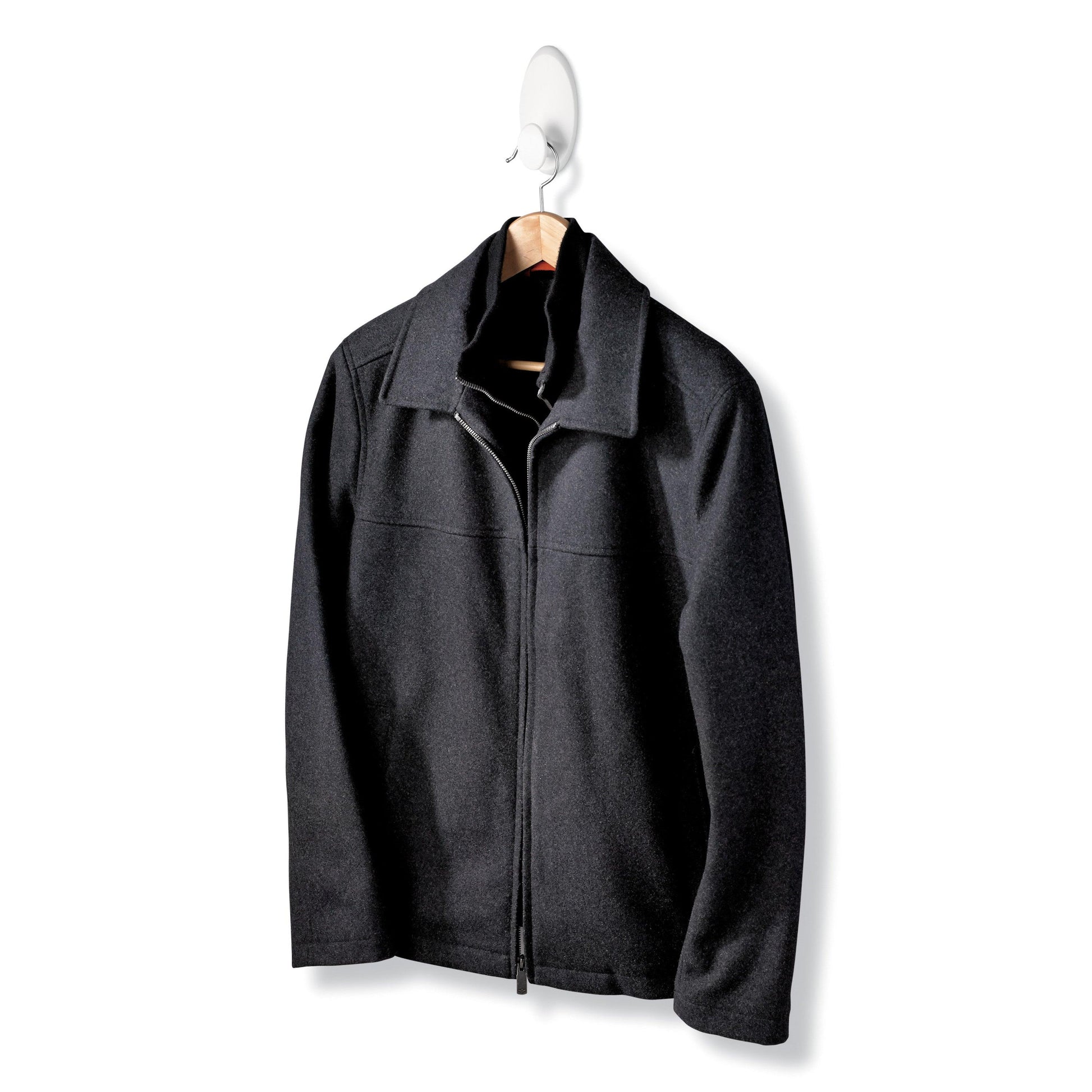Eine schwarze Jacke mit Reißverschluss und Kragen hängt an einem Holzbügel des Command™ Kleider-Hakens, 17019-FGN, der eine Wandbefestigung ohne Bohren ermöglicht, vor einem schlichten weißen Hintergrund.