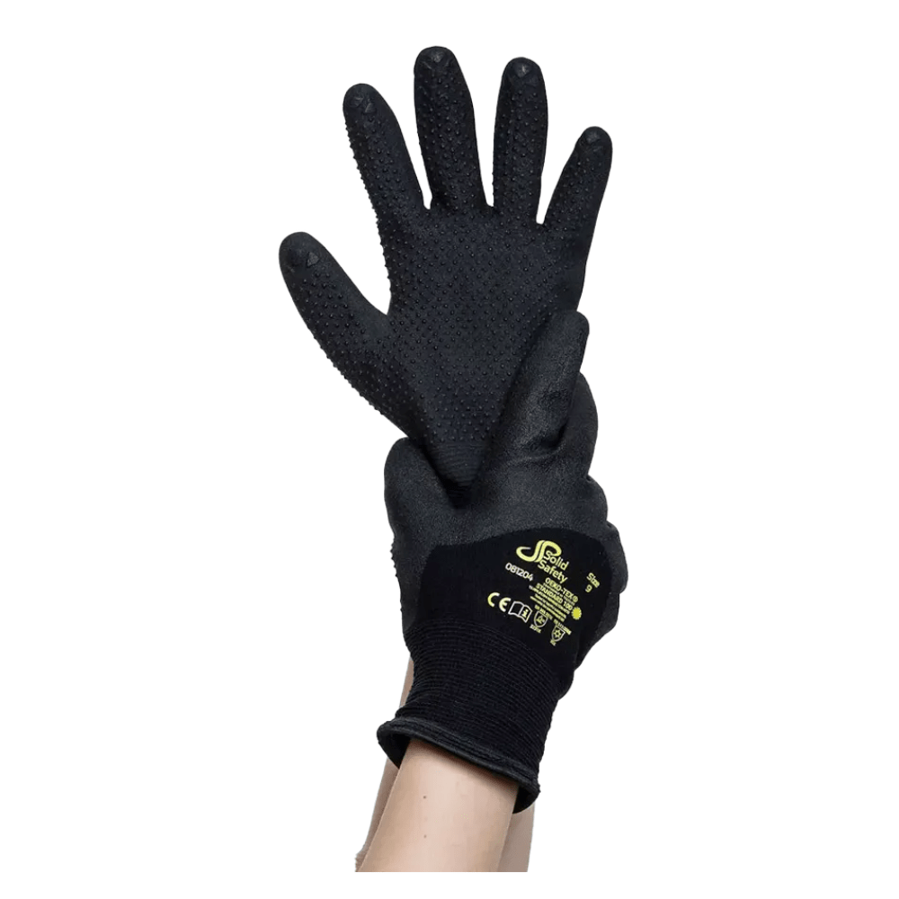 Ένα ζευγάρι μαύρα AMPri SolidSafety Tough Winter Dots Ανθεκτικά στο κρύο προστατευτικά γάντια με δομημένες παλάμες κρατιέται ψηλά από ένα χέρι. Αυτά τα γάντια, που προορίζονται να βελτιώσουν τη λεπτή κινητικότητα, φέρουν στο πίσω μέρος το κίτρινο σήμα κατατεθέν και τα σημάδια πιστοποίησης ασφαλείας της AMPri Handelsgesellschaft mbH.