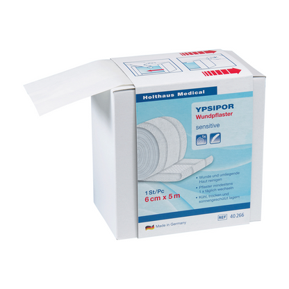 Απεικονίζεται ένα κουτί Holthaus Ypsipor Wundpflaster Vlies της Holthaus Medical GmbH & Co. KG. Στο κουτί αναγράφεται ότι είναι ευαίσθητο, μετρά 6 cm x 5 m και κατασκευάζεται στη Γερμανία. Ένα μέρος της φιλικής προς το δέρμα Vlies-Wundverbandrolle είναι ορατό και προεξέχει από το κουτί.