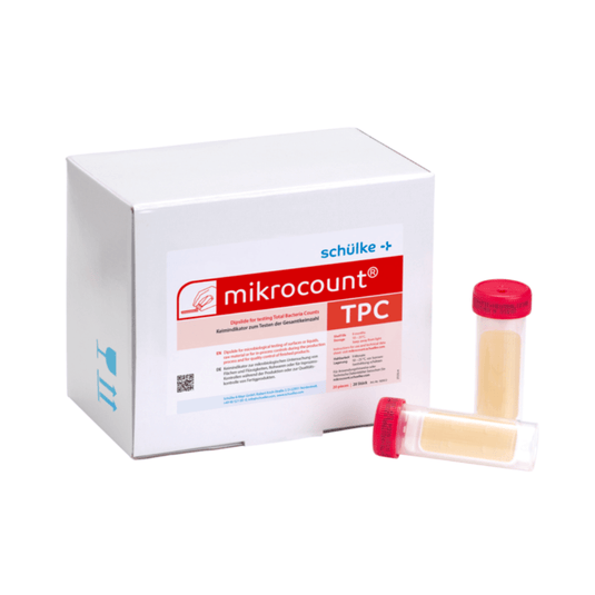 Ένα λευκό κουτί με την ένδειξη «Schülke & Mayr GmbH Mikrocount® TPC, θρεπτικό υπόστρωμα | Συσκευασία (20 τεμάχια)», με ένα λογότυπο και μια περιγραφή του προϊόντος, δίπλα σε δύο φιαλίδια για μικροβιακές δοκιμές, το ένα με κίτρινο καπάκι και το άλλο με διαφανές καπάκι.