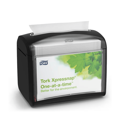Ένας μαύρος διανομέας χαρτοπετσετών Tork Xpressnap® 272611, που διανέμεται από την TORK – Essity Professional Hygiene Germany GmbH, παρουσιάζεται με μια ετικέτα με πράσινα φύλλα και το μήνυμα «Μία-μία. Καλύτερα για το περιβάλλον». Μια μεμονωμένη χαρτοπετσέτα εκδίδεται μερικώς από πάνω για να προάγει την υγιεινή και την αποδοτική κατανάλωση χαρτοπετσετών.