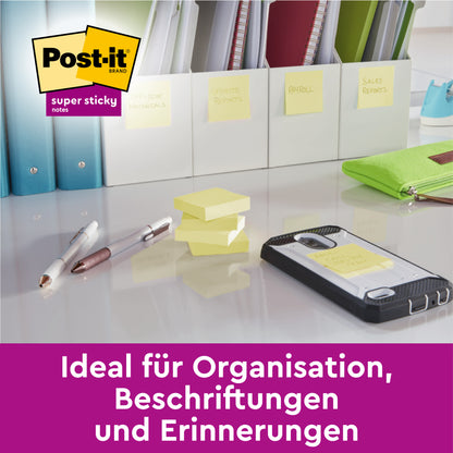 Ein Schreibtisch mit Stiften, Telefon, gestapelten Post-it® Super Sticky 100 % Recycling Notes (76x76 mm, 70 Blatt/Block, 100% PEFC) und mit diesen Notizen beschrifteten Ordnern von 3M Deutschland GmbH - ideal für Organisation und Erinnerungen.