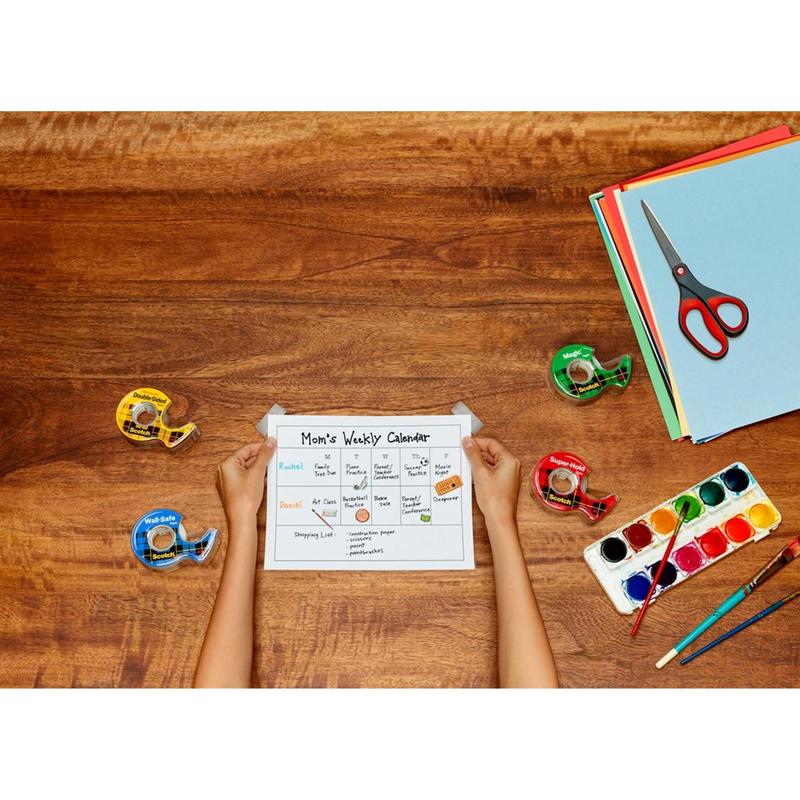 Ένα άτομο κρατάει ένα "Mom's Weekly Calendar" σε ξύλινο τραπέζι με τέσσερις αποσπώμενες ταινίες, χρωματιστό χαρτί, ένα σετ ακουαρέλας με πινέλο και ένα κόκκινο ψαλίδι ακρίβειας Scotch™ από την 3M Deutschland GmbH.