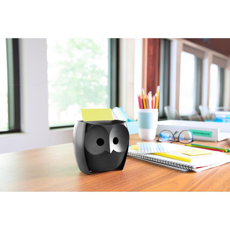 Ένας διανομέας Post-it® Z-Notes, κουκουβάγια, μαύρος της 3M Deutschland GmbH βρίσκεται σε ένα ξύλινο τραπέζι με σημειωματάρια, μια κούπα, χρωματιστά μολύβια σε μια κούπα και Post-it® Super Sticky Z-Notes (45 φύλλα/μπλοκ, 2 μπλοκ/συσκευασία). Μεγάλα παράθυρα δίνουν θέα σε δέντρα.