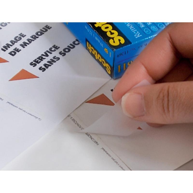 Ένα χέρι τραβά ένα τριγωνικό αυτοκόλλητο από ένα φύλλο με την επιγραφή "IMAGE DE MARQUE SERVICE SANS SOUCI", ενώ στο φόντο υπάρχει ένα κουτί με αόρατη ταινία Scotch® από την 3M Deutschland GmbH, αφαιρούμενη, 19 mm x 33 m, 1 ρολό | 1 κομμάτι.
