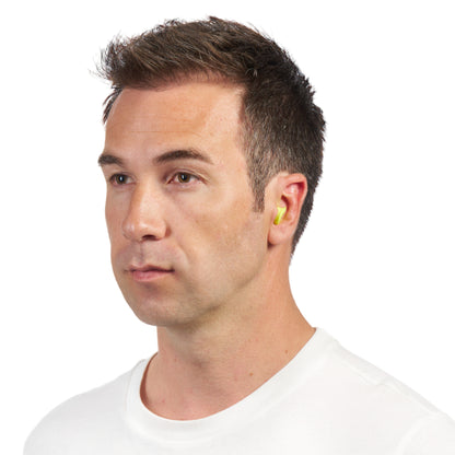 Eine Nahaufnahme zeigt einen Mann mit kurzen braunen Haaren und weißem T-Shirt, der leicht nach links schaut und einen gelben 3M™ Gehörschutzstöpsel E-A-Rsoft™ FX™ (SNR-Wert 37 dB, weicher Polyurethanschaum) der 3M Deutschland GmbH in seinem rechten Ohr trägt.