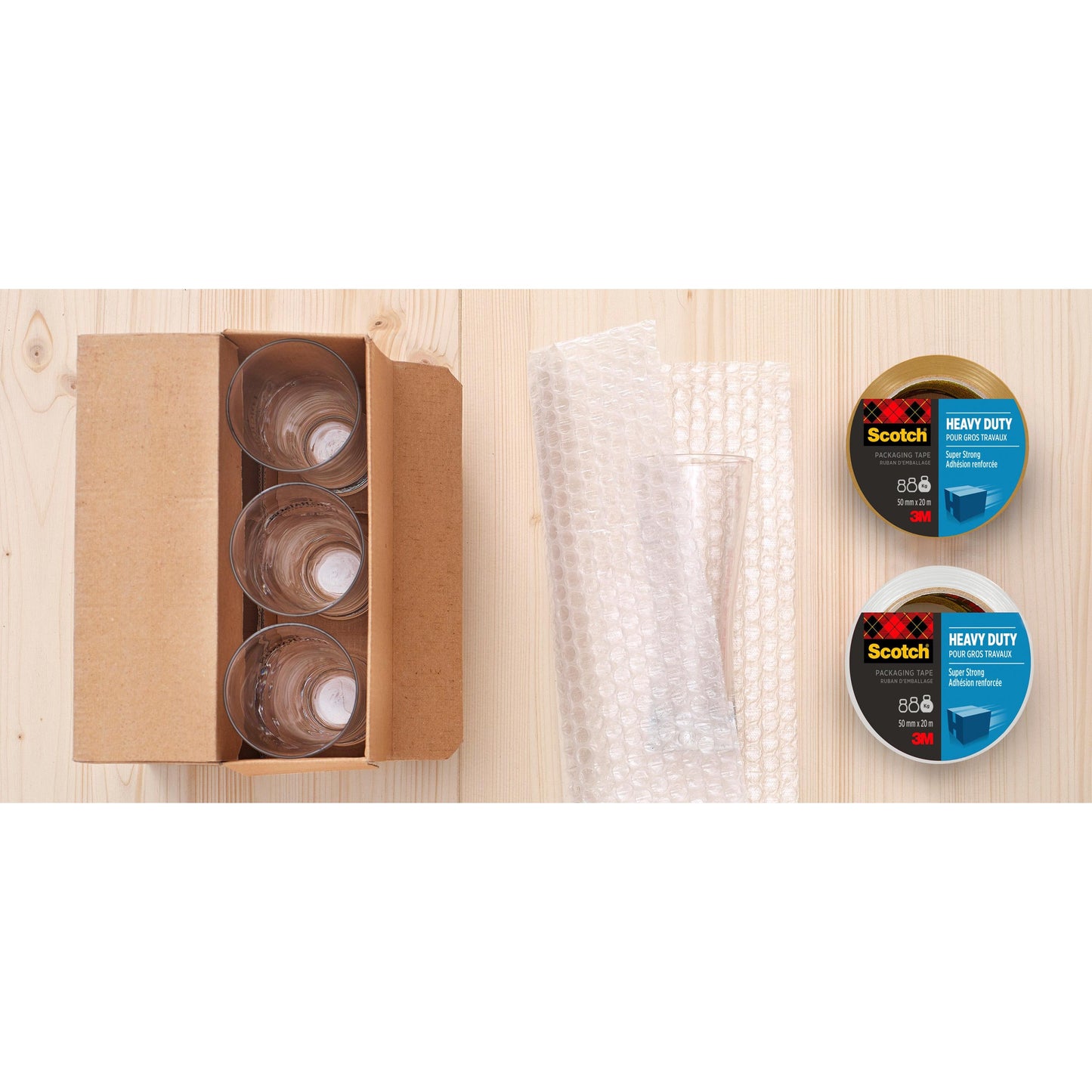 Vier Glasbecher in einem Karton, Luftpolsterfolie und zwei Rollen Scotch® Extra starkes Verpackungsklebeband (3M Deutschland GmbH, transparent, 48 mm x 20 m) werden auf einer hellen Holzfläche angeordnet.