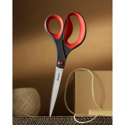 Ένα ζευγάρι κόκκινων ψαλιδιών ακρίβειας Scotch™ από την 3M Deutschland GmbH είναι κολλημένο όρθιο σε χαρτόνι κυματοειδούς, στο φόντο διακρίνονται μπεζ κορδόνια και ένα κουτί.