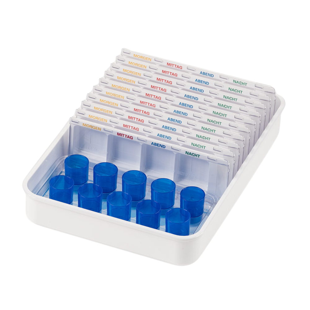 Ένας λευκός δίσκος-ποτήρι-δοσομετρικό σύστημα Melipul από την Helmut Schwarz GmbH περιέχει πολλούς διαφανείς διανεμητές χαπιών, μέρος ενός συστήματος οργάνωσης φαρμάκων, με ετικέτες στα γερμανικά για την ώρα της ημέρας: «Πρωί», «Μεσημέρι», «Βράδυ», «Νύχτα». Κάθε επαναχρησιμοποιούμενος διανεμητής διαθέτει σχισμές για χάπια και μπλε καπάκια στη μία πλευρά.